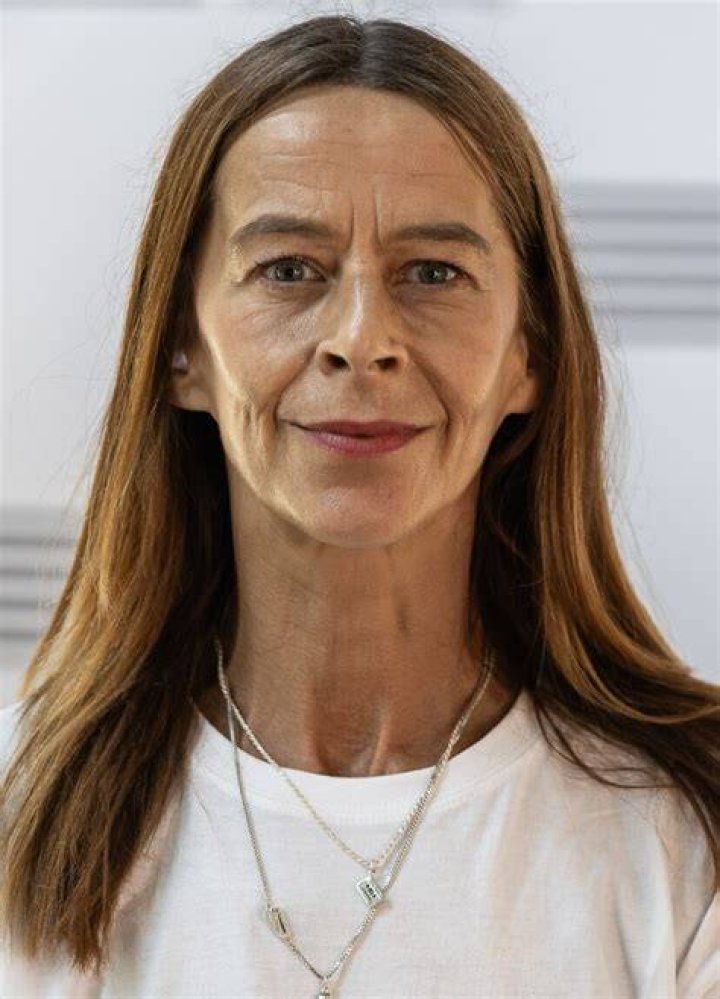 Kate Dickie standing in front of a green and yellow background wearing a forest green button up jacket
