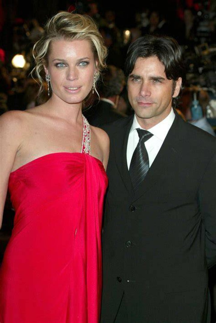 Rebecca Romijn and John Stamos pose for a photo together, smiling. 